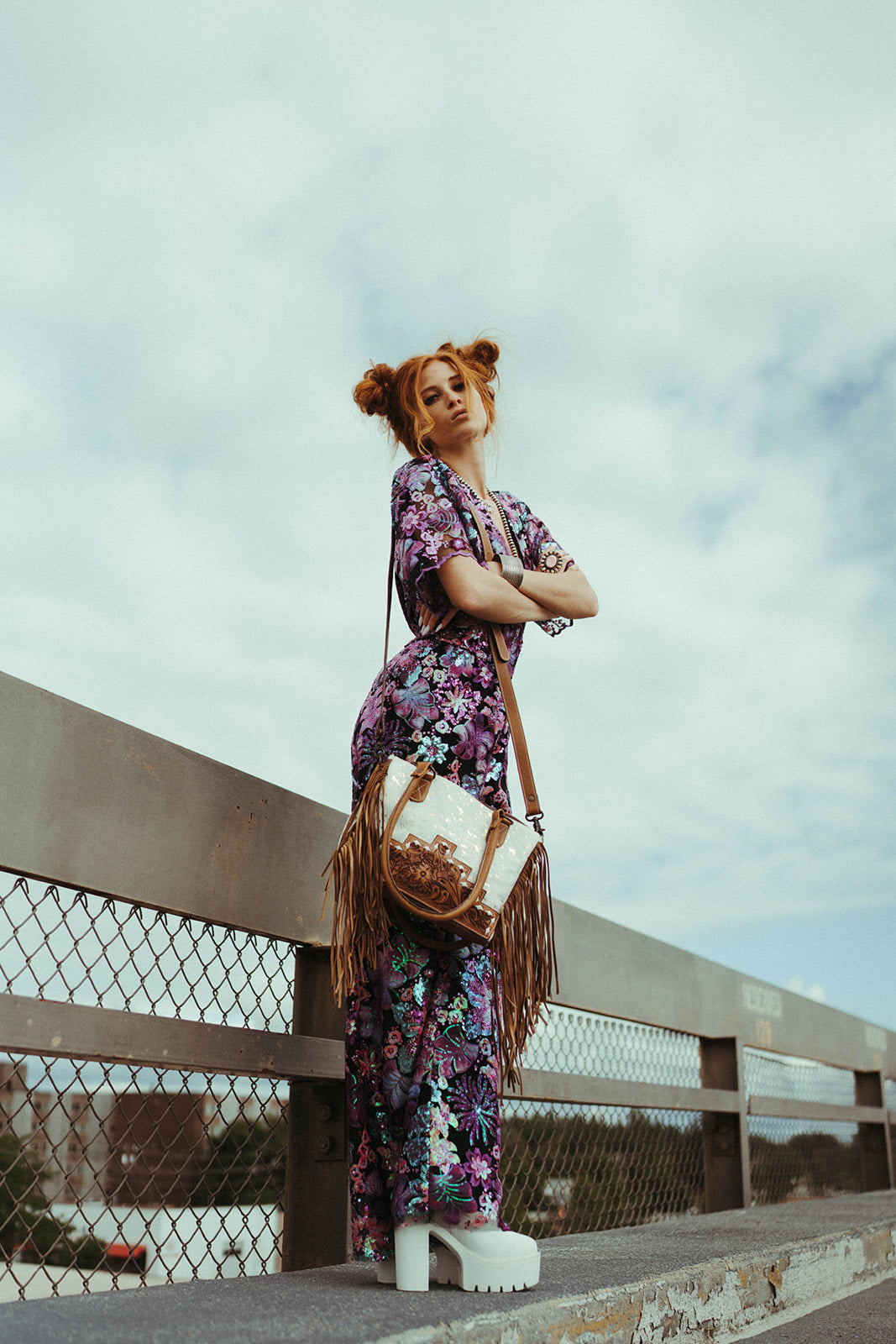Woman in a floral dress standing on a bridge with a cloudy sky.