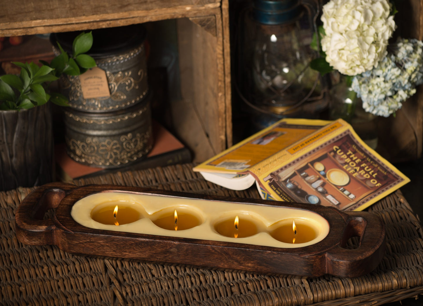 Wax melt around 4 lit candles on a wooden tray surface with decorative items on a shelf or table.