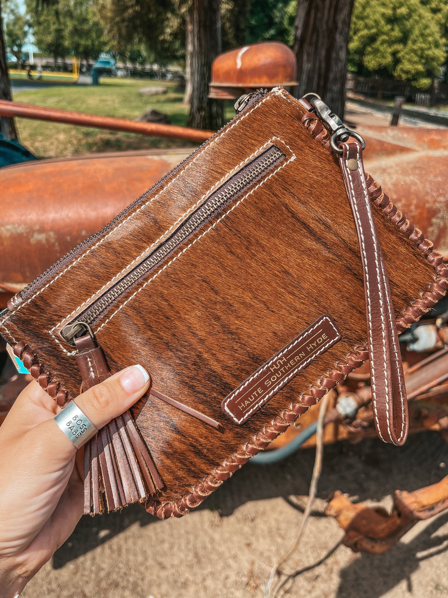 Brown leather clutch held by a hand with a blurred outdoor background