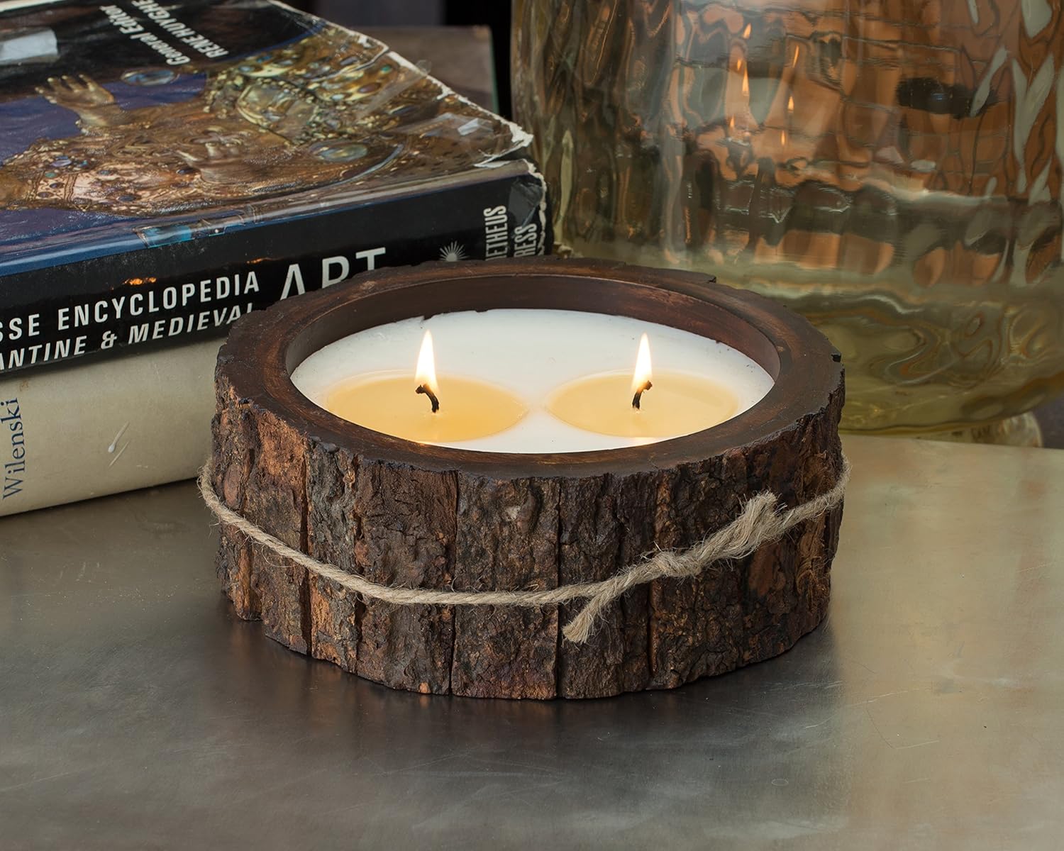 Wooden candle holder with tree bark surface with two lit wicks on a reflective table top surface.