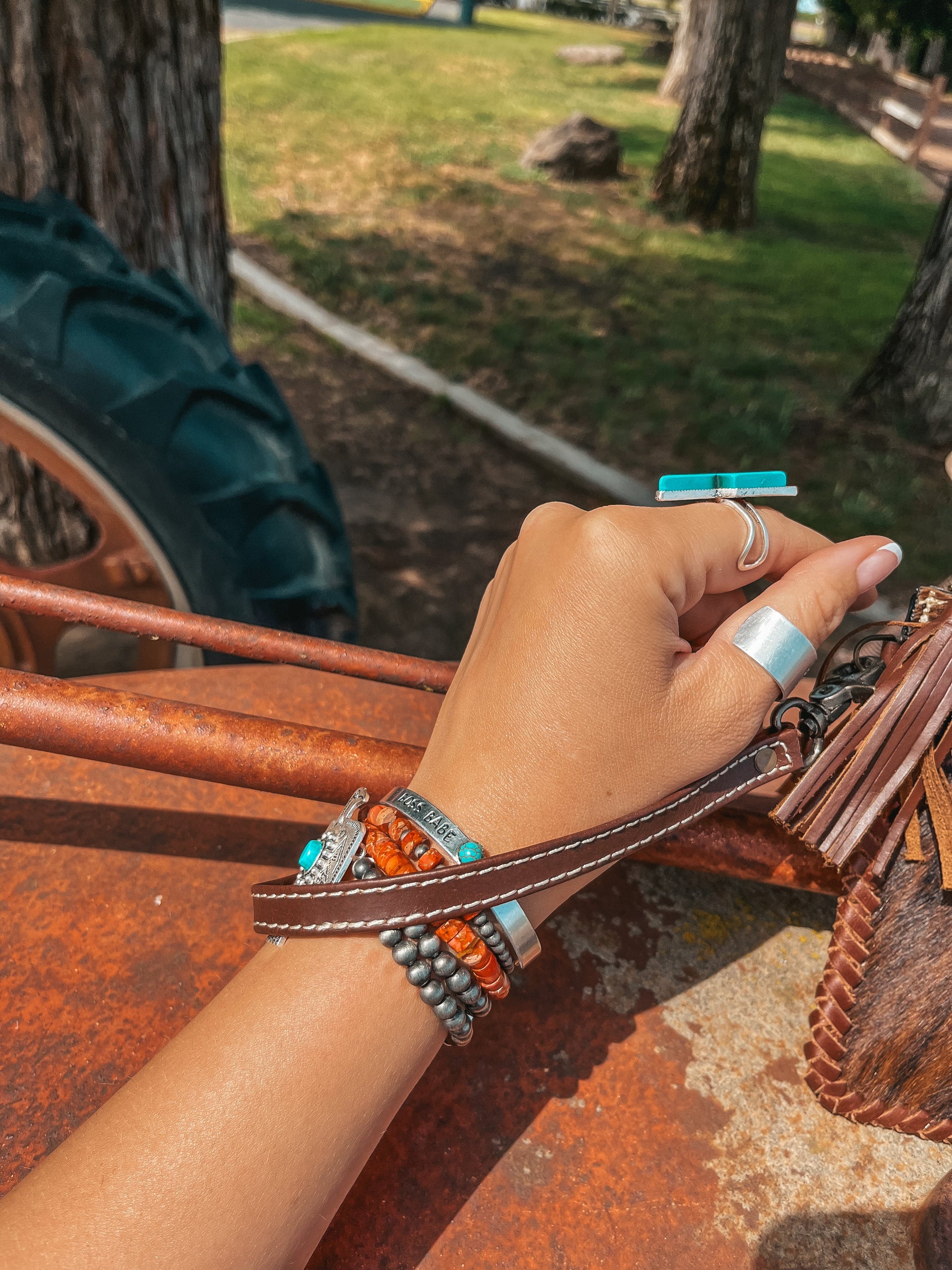Hand wearing multiple bracelets with a blurred outdoor background