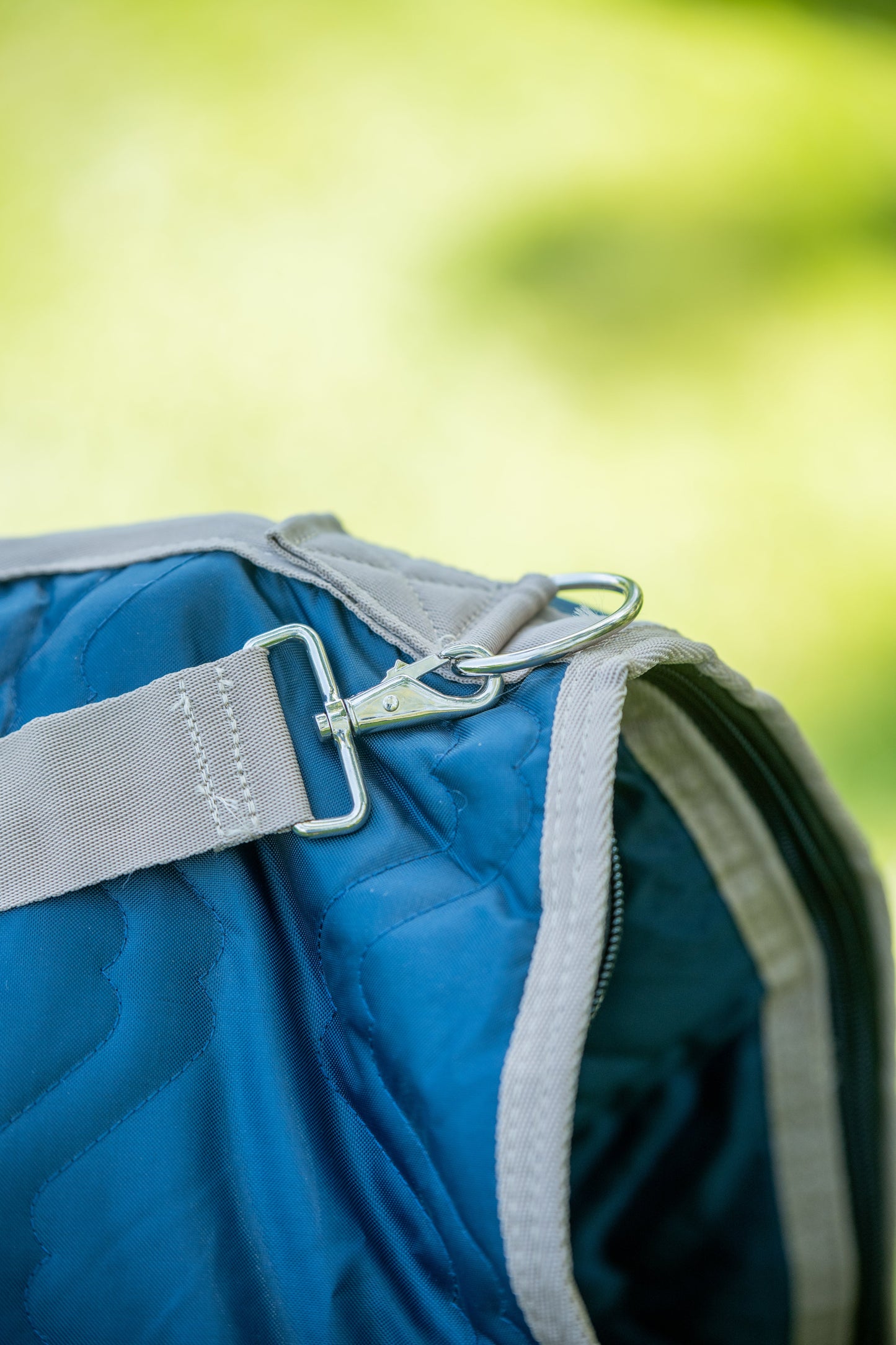 Close-up of a blue saddle bag carrier with a gray strap and carabiner against a blurred green background