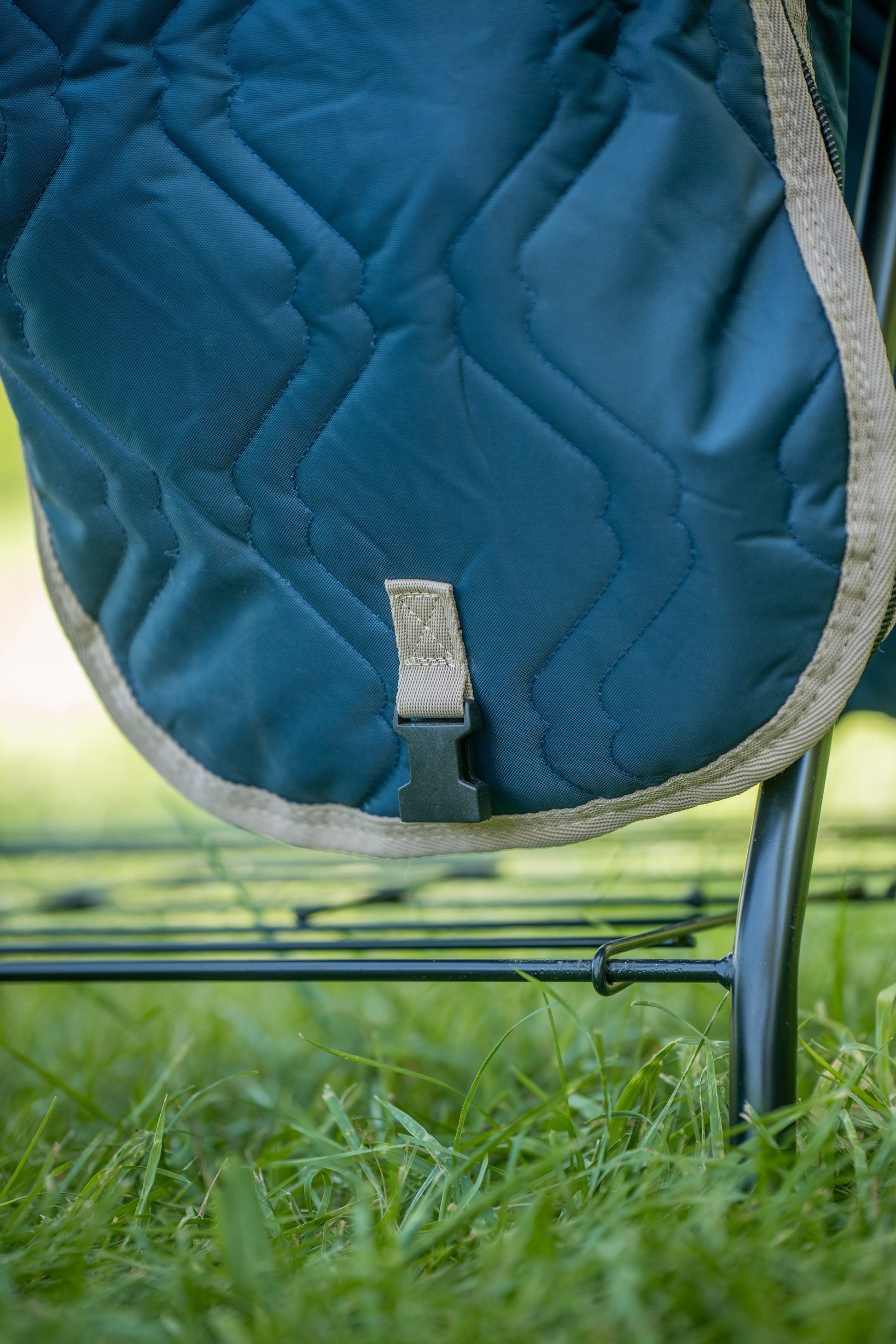 Blue quilted saddle bag carrier on a metal frame with grass in the background