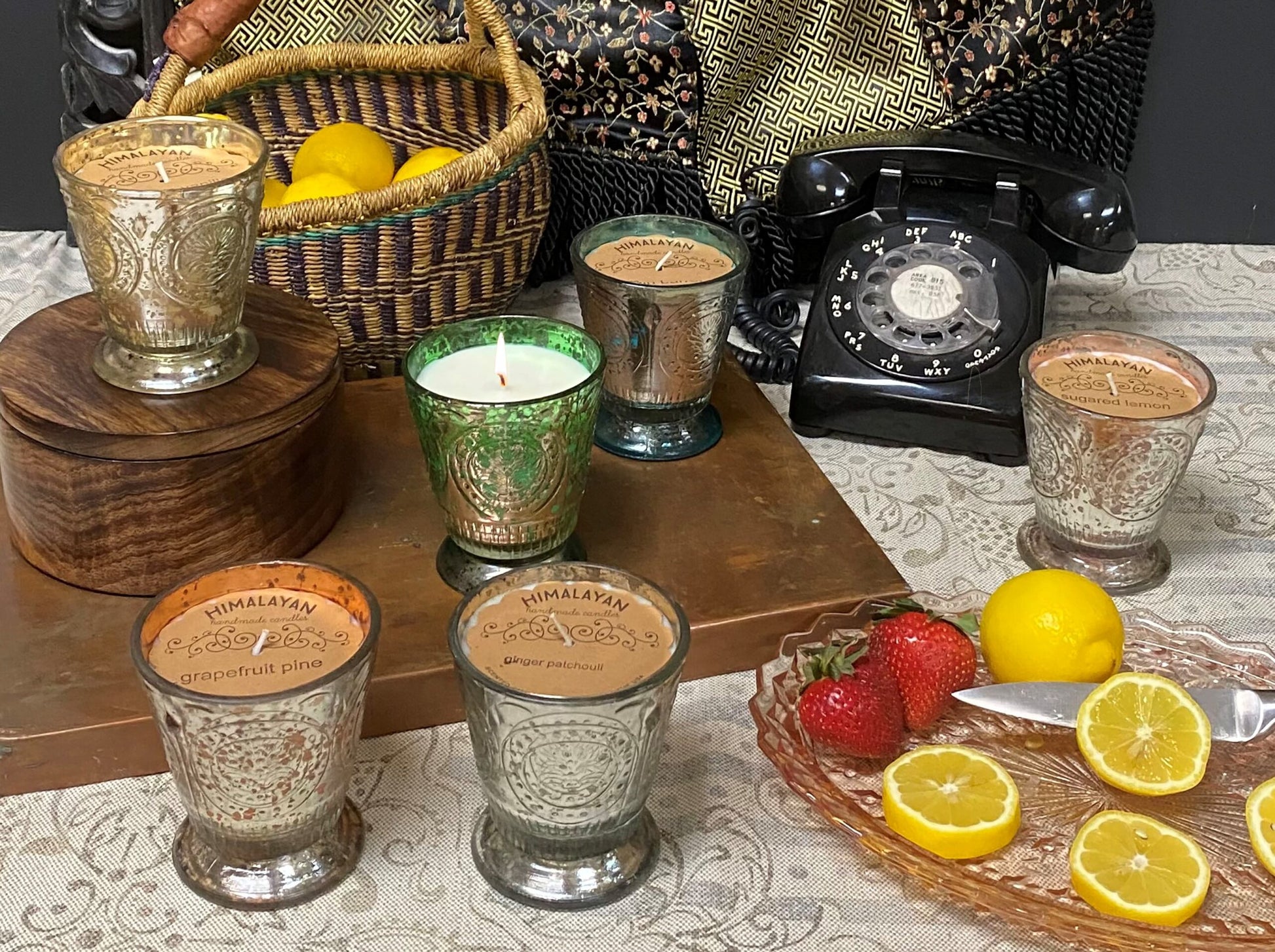Decorative setting with candles, lemons, strawberries, and a vintage phone on a table.