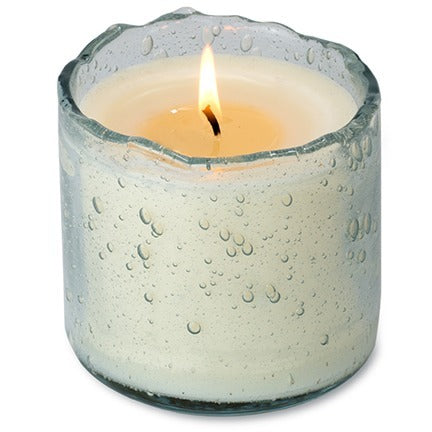 Candle in a textured glass holder with water droplets on a white background