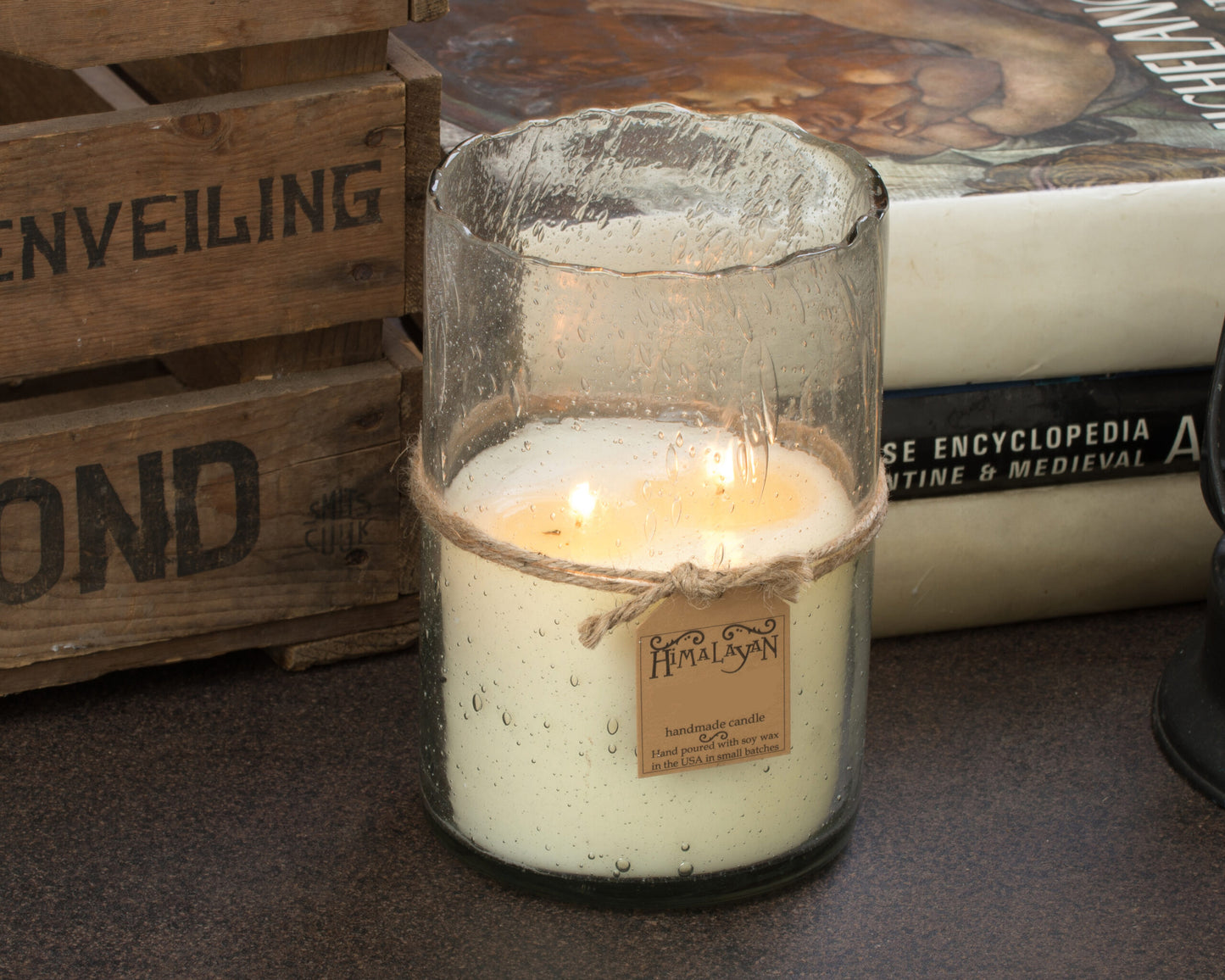 Candle in a glass container with a wooden crate and book in the background