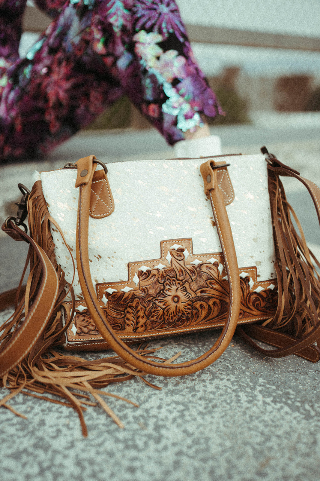 White western handbag with brown leather accents and floral patterns on a textured surface.