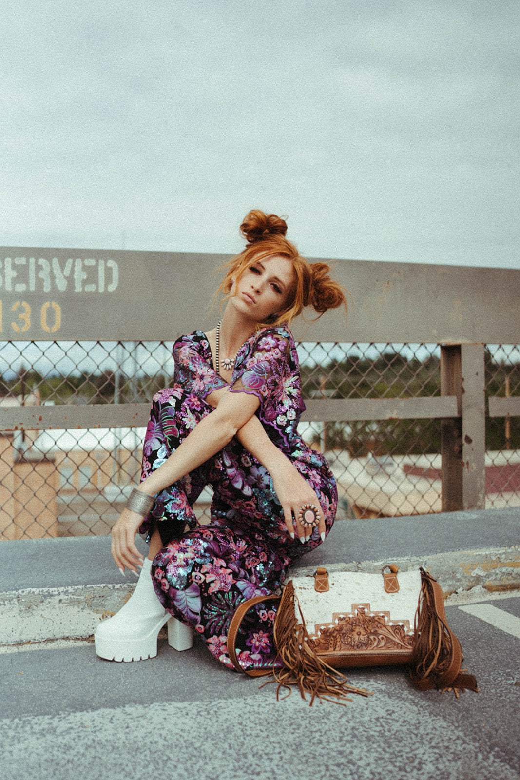 Woman in a floral dress sitting on a bench with a western handbag, outdoors.