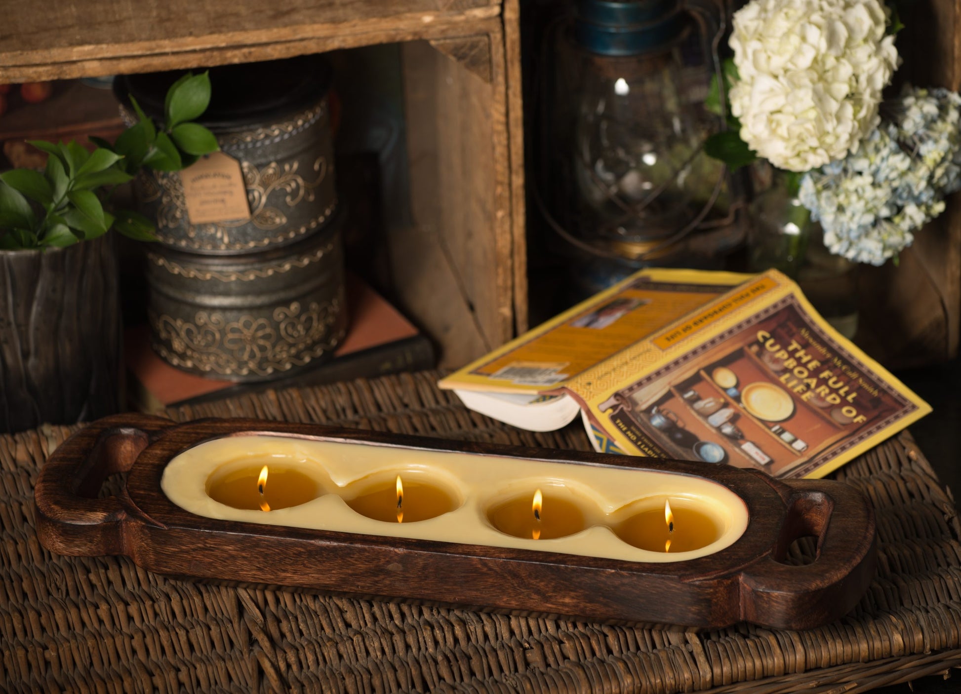 Wax melt around 4 lit candles on a wooden tray surface with decorative items on a shelf or table. 