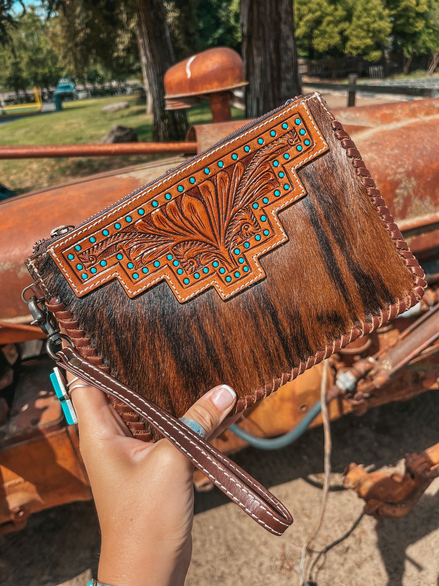 Brown leather clutch with intricate designs held by a hand, with a rustic background.