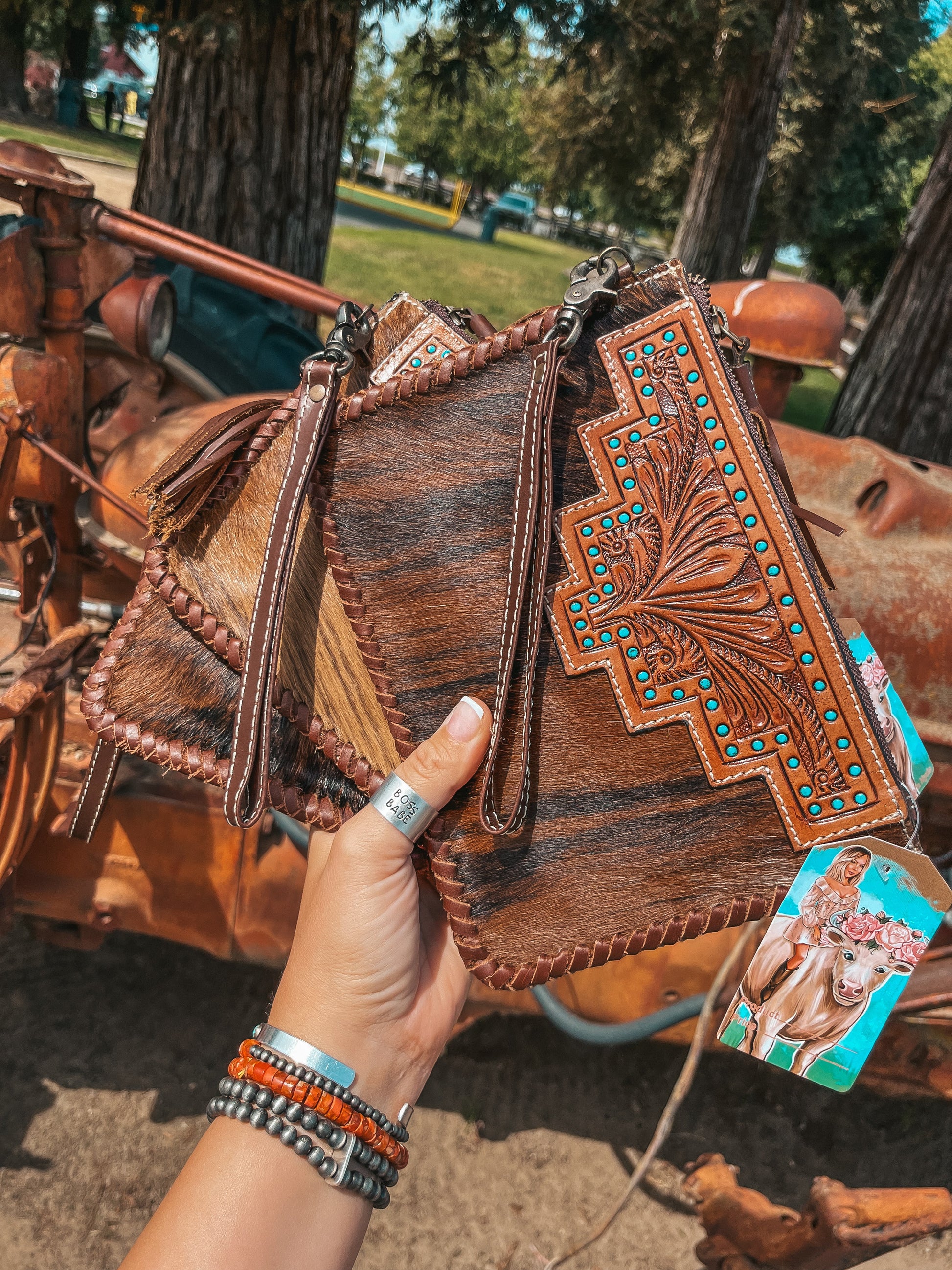 Hand holding a decorative leather clutch with intricate designs, outdoors.